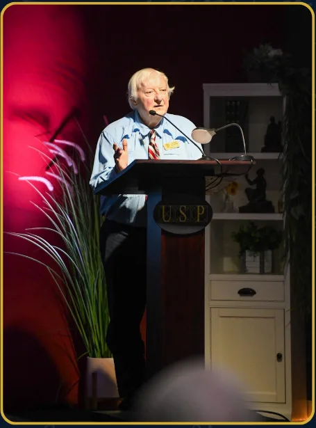 A speaker presenting at a USP podium under warm stage lighting.